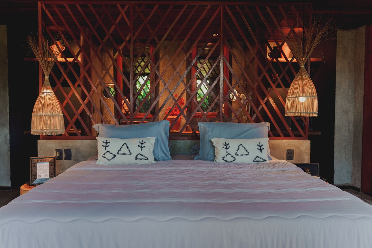 Un grand lit avec une couvre-lit rayée blanche et rose, deux oreillers bleus et une tête de lit décorative ornée d’un motif en treillis.