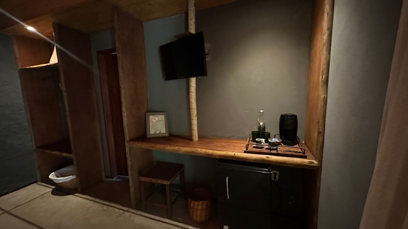 A compact kitchen with a wooden countertop, a small stool, a coffee machine, and a television mounted on the wall.