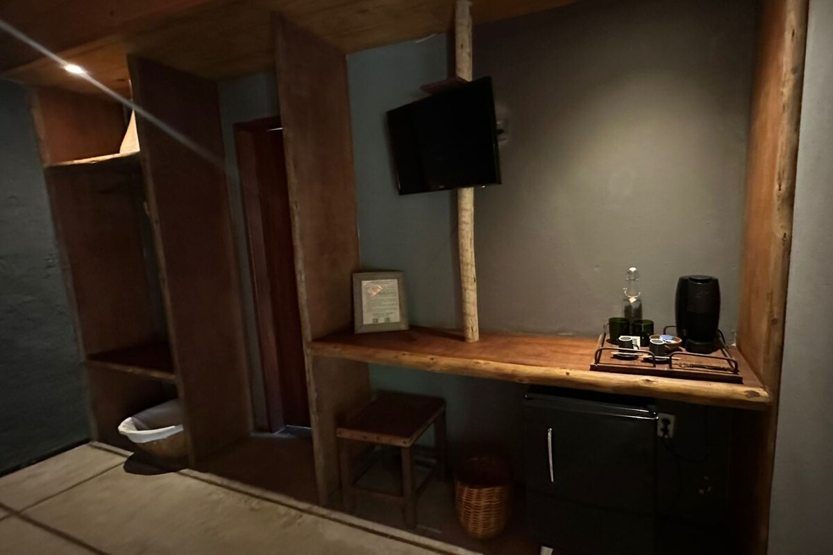 A compact kitchen with a wooden countertop, a small stool, a coffee machine, and a television mounted on the wall.