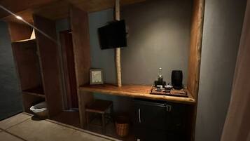 Cocina compacta con encimera de madera, un taburete pequeño, una cafetera y un televisor fijado a la pared.