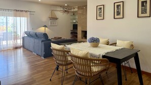 A modern living room with a sofa, dining table, wicker chairs, and a fireplace. - BELLA CENA by Azores HomeMade (Ponta Delgada)