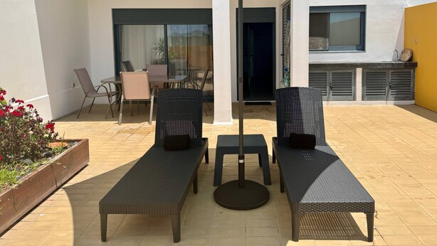 A patio with two lounge chairs, a table, and a large umbrella. - BELLA CENA by Azores HomeMade (Ponta Delgada)