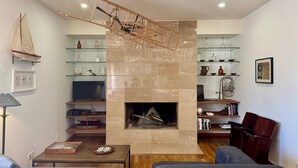 A living room with a fireplace, wooden shelves, a television, and a sailboat model. - BELLA CENA by Azores HomeMade (Ponta Delgada)