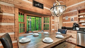 A wooden cabin interior with a dining table set for four, a kitchen area, and large windows offering a forest view. - FreeDollywood Tix/Secluded/Pool Table/Spacious (Gatlinburg)