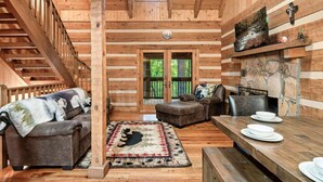 A log cabin interior with a wooden staircase, a sofa, a dining table with plates, and a fireplace. - FreeDollywood Tix/Secluded/Pool Table/Spacious (Gatlinburg)