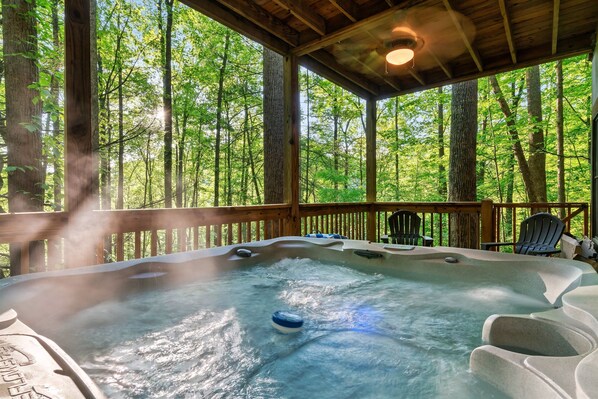 A hot tub on a wooden deck with a forest view.