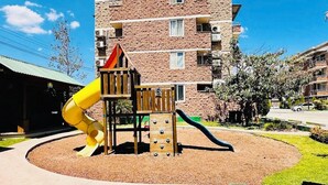 A playground with a yellow slide and climbing area, surrounded by a landscaped garden and a multi-story building in the background. - Beautiful private apartment Ecovivienda Etapa 1 (8 minutes American Embassy) (Tegucigalpa)