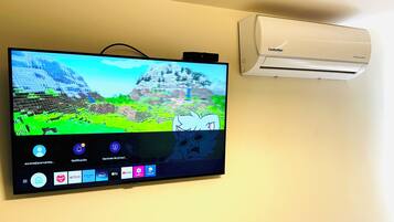A flat-screen TV mounted on a wall with a white air conditioning unit beside it.