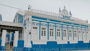 Un edificio con fachada azul y blanca, barandillas blancas ornamentadas y un techo decorativo.