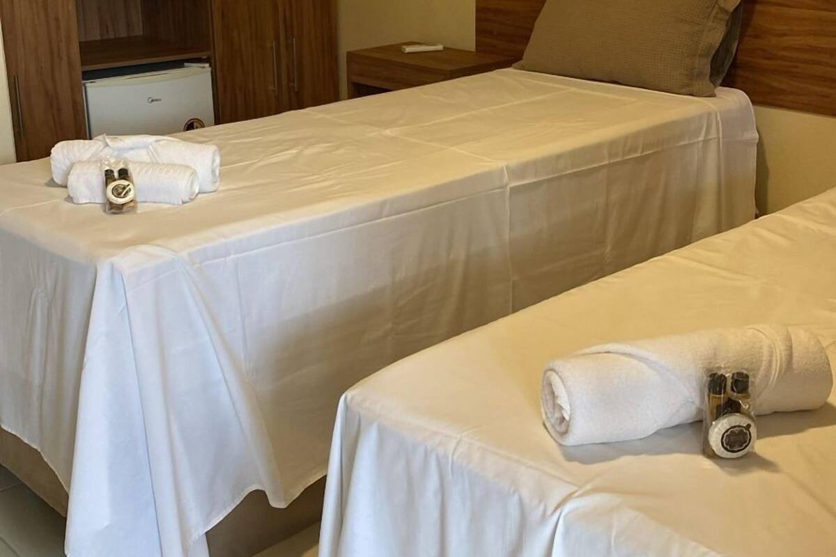 Two single beds with white linens, a wooden headboard, a small bedside table, and a minibar.