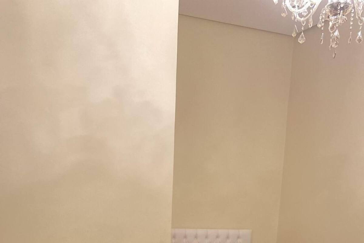 A hotel room with three beds, each with a white mattress and brown headboard. There is a wooden floor and a chandelier hanging from the ceiling.
