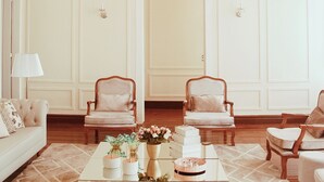 Una sala de estar formal con una araña, dos sillones, un sofá y una mesa de centro con adornos.