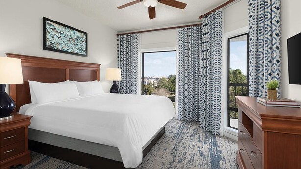 A hotel room with a large bed, two bedside tables with lamps, a ceiling fan, patterned curtains, and a view of the outdoors. - Marriott's Harbour Point - Hilton Head Island
2 Bedroom Villa (Hilton Head Island)