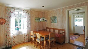 Un coin repas avec une table et des chaises en bois, un luminaire suspendu et une fenêtre agrémentée de rideaux à motifs floraux.