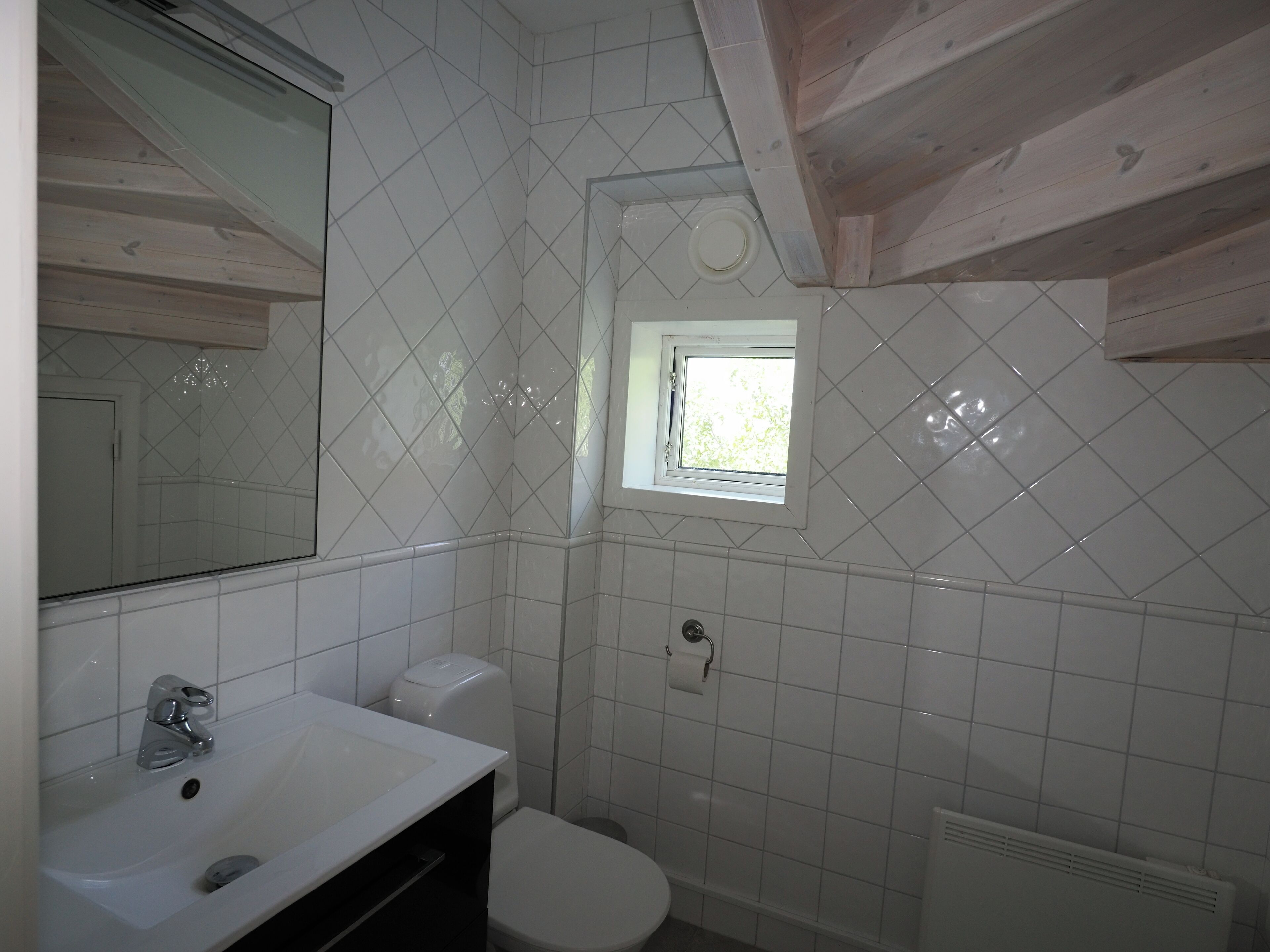 A bathroom with a white sink, toilet, and a window above the toilet.
