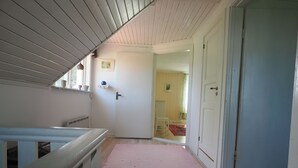 Un couloir avec un tapis rose, des murs blancs et une porte donnant sur une autre pièce.