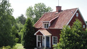 Une maison rouge avec un toit en pente, un porche à l’avant et une allée gravillonnée.