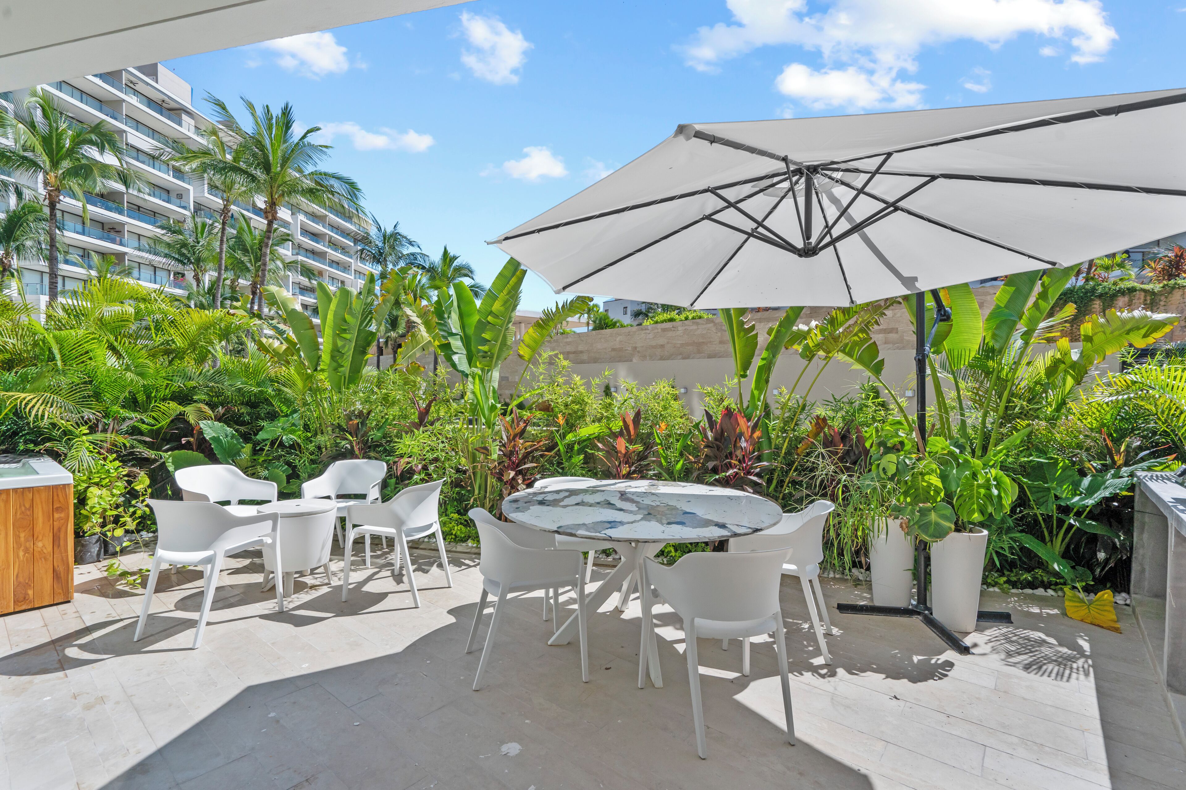 An outdoor patio with a round table, white chairs, and a large umbrella.