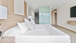 Ein modernes Hotelzimmer mit einem großen Bett, einem Nachttisch, einer Lampe und Blick auf die Stadt durch eine Glastür.