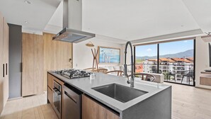 Eine moderne Küche mit einer zentralen Kochinsel, Edelstahlgeräten und einem großen Fenster mit Blick auf eine Wohngegend.