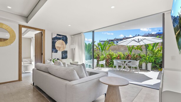 Ein modernes Wohnzimmer mit einer Couch, einem runden Couchtisch und Blick auf die Terrasse mit Stühlen und Sonnenschirmen.