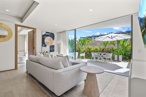 A modern living room with a sofa, a round coffee table, and a view of the outdoor patio area with chairs and umbrellas. - Nima Bay Oasis (Puerto Vallarta)