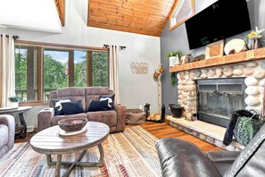 Een gezellige woonkamer met een open haard, comfortabele zitplaatsen en een groot raam.