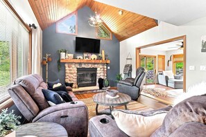 Ein modernes Wohnzimmer mit Kamin aus Stein, Ledersofas, einem runden Couchtisch und einem großen Fernseher, der über dem Kamin angebracht ist.