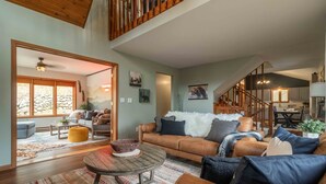 A spacious living room with a brown sofa, a coffee table, and a dining area with wooden furniture.
