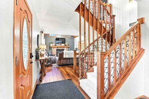 Eine Holztreppe mit Metallgeländer führt zu einem Wohnbereich mit Kamin, Sofa und Fernseher.
