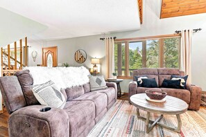 Ein Wohnzimmer mit Sofa, Sessel und Couchtisch. Ein Fenster mit Jalousien, eine Lampe und ein dekorativer Spiegel sind ebenfalls vorhanden.