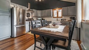 A modern kitchen with stainless steel appliances, grey cabinets, and a wooden dining table.