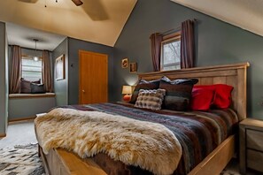 Ein Schlafzimmer mit einem großen Bett, einem Holz-Kopfteil, einem Fenster mit Vorhängen, einer Wandlampe und einer Tür.