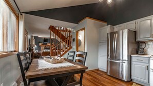 A modern kitchen with a stainless steel refrigerator, wooden dining table, and chairs.