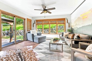 A modern living room with a sofa, armchairs, a coffee table, and a view of a garden through large windows.
