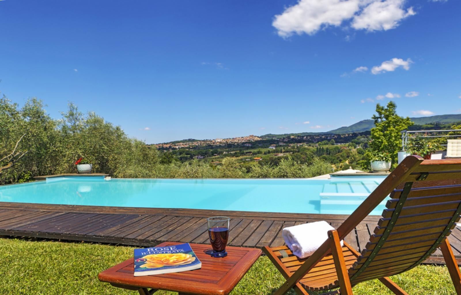 A wooden deck with a pool, a lounge chair, a glass of drink, and a book titled "Rose Neustrat".