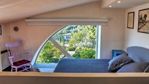 A bedroom with a large window, a bed, a rocking chair, and a small table.