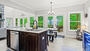Una cocina moderna con una isla central, ventanas amplias y un comedor con mobiliario de exterior.