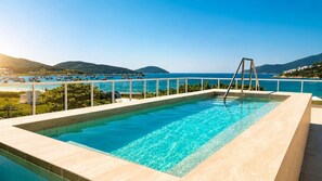 A rectangular pool with clear blue water, surrounded by a white railing, overlooking a coastal area with boats and hills. - Arraial Concept Hotel E Spa (Arraial do Cabo)