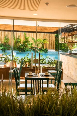 A dining area with a view of a pool and greenery, featuring a table with chairs and a bar counter. - Arraial Concept Hotel E Spa (Arraial do Cabo)