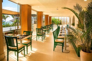 A restaurant with green chairs and tables, large windows, and potted plants. - Arraial Concept Hotel E Spa (Arraial do Cabo)
