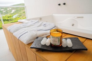 A spa area with a bathtub, towels, a candle, and essential oils on a wooden table. - Arraial Concept Hotel E Spa (Arraial do Cabo)