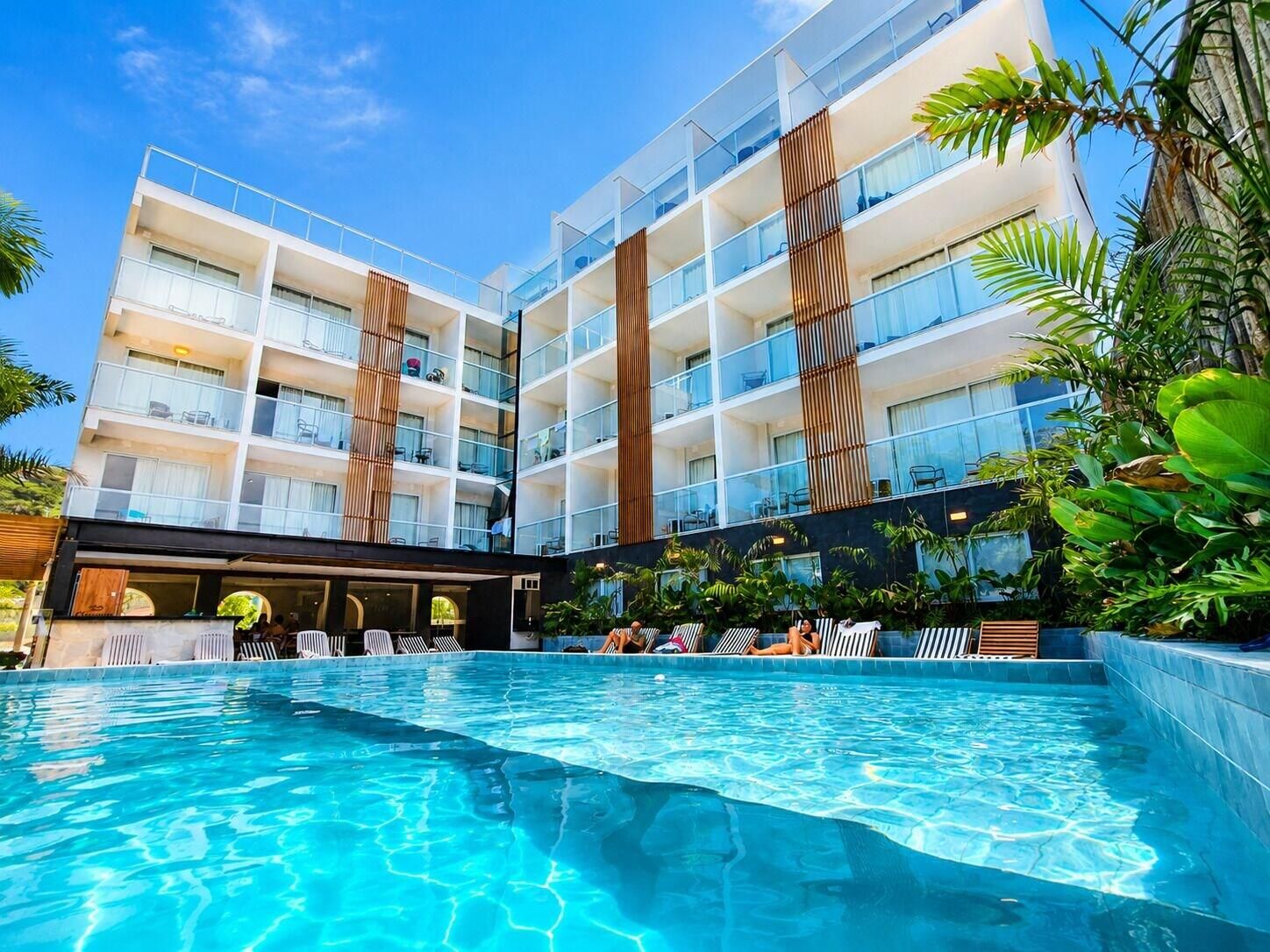 A hotel with a swimming pool, multiple balconies, and lush greenery.