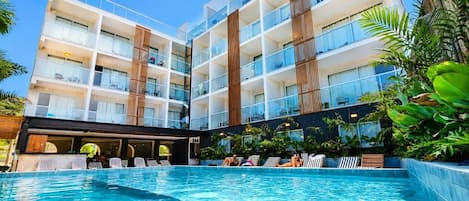 A hotel with a swimming pool, multiple balconies, and lush greenery.