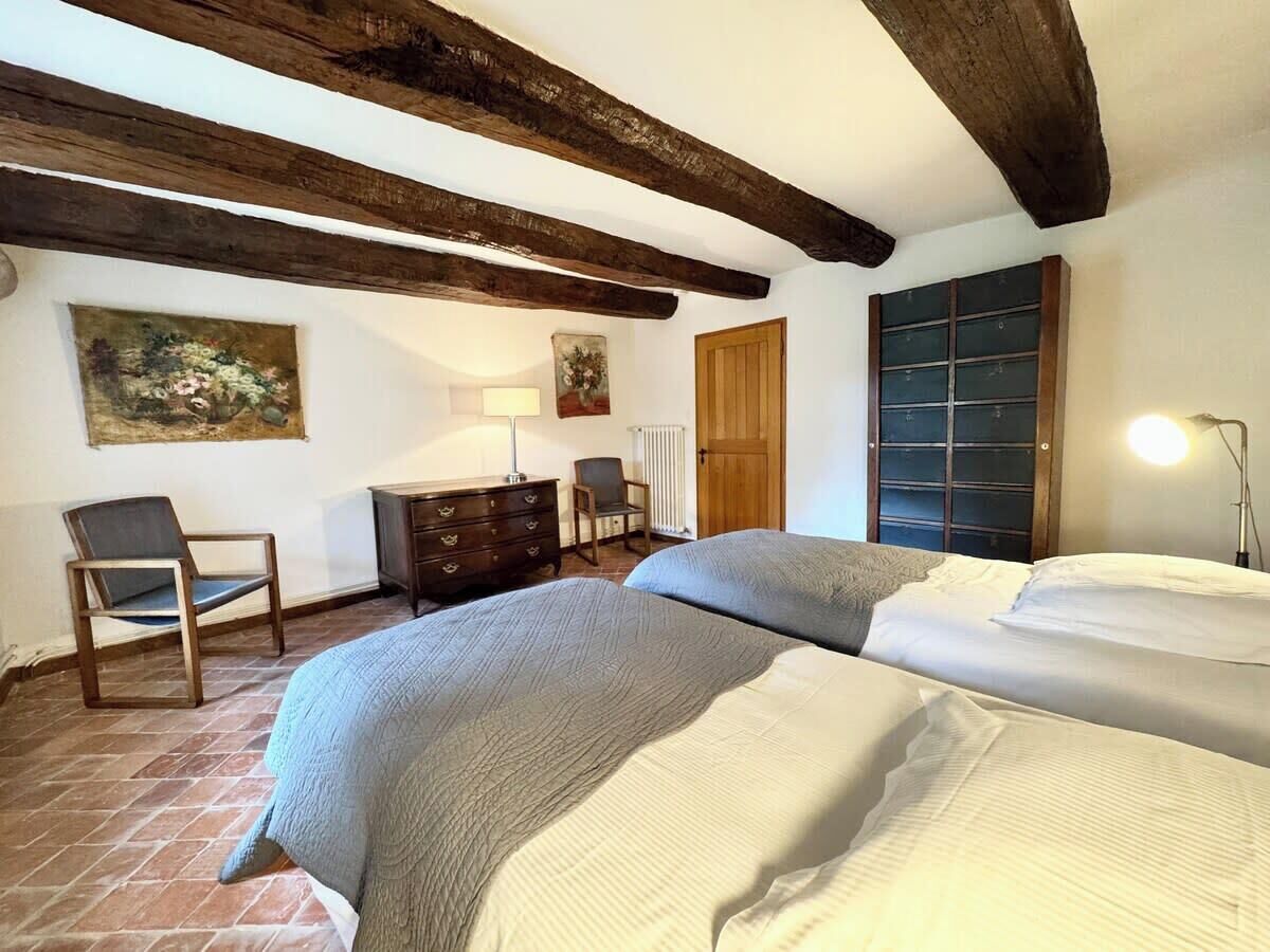 A bedroom with two beds, wooden beams on the ceiling, a dresser, a chair, and a radiator.