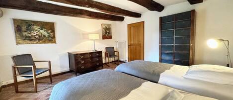 A bedroom with two beds, wooden beams on the ceiling, a dresser, a chair, and a radiator.