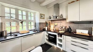 Una cocina con armarios blancos, encimera negra y horno empotrado. Se ven ventanas con vistas a zonas verdes.