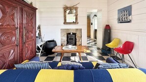 A cozy living room with a checkered floor, a fireplace, a wooden table, and colorful chairs.