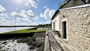 A stone building with a wooden deck overlooking a body of water.