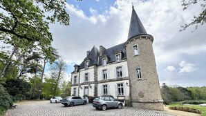 A historic stone building with a turret, a cobblestone driveway, and parked cars.